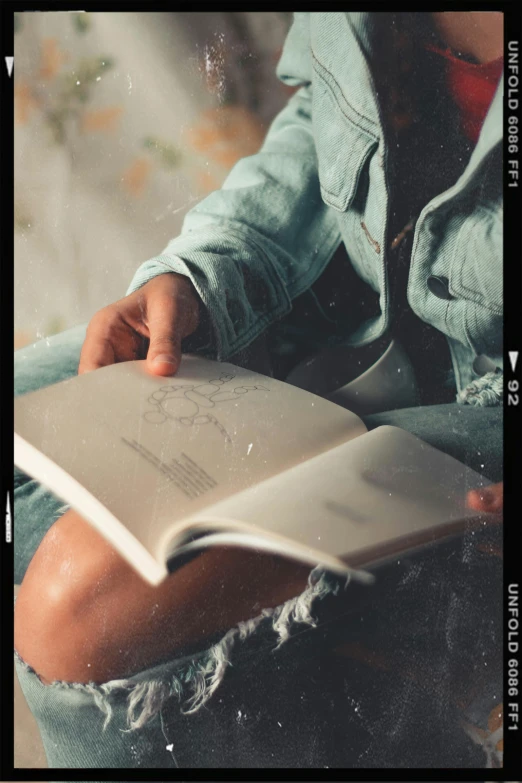 a person sitting on a bed reading a book, an album cover, by Niko Henrichon, trending on pexels, faded, denim, village girl reading a book, grainy footage