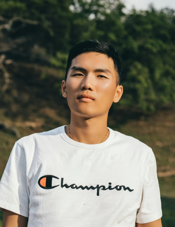 a man wearing a white t - shirt with the word champion on it, inspired by Ryan Yee, androgynous face, trending on vsco, asian descent, ☁🌪🌙👩🏾