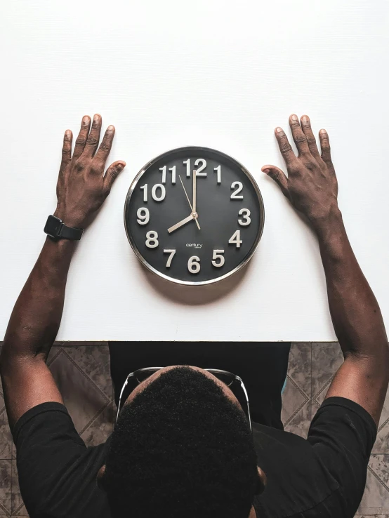 a man holding a clock above his head, trending on unsplash, man is with black skin, hand on table, realistic »