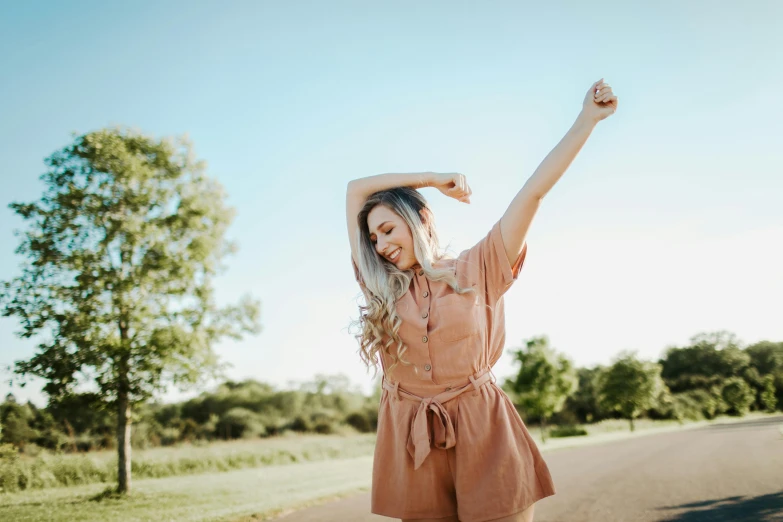 a woman standing on a road with her arms in the air, a portrait, trending on pexels, muted colored bodysuit, orange jumpsuit, tan skin a tee shirt and shorts, sydney sweeney