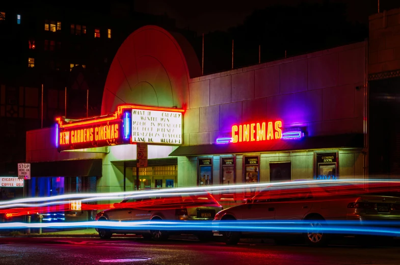 a car driving past a movie theater at night, by Peter Churcher, unsplash contest winner, red and blue neon, seattle, cinamtic, pink and orange neon lights