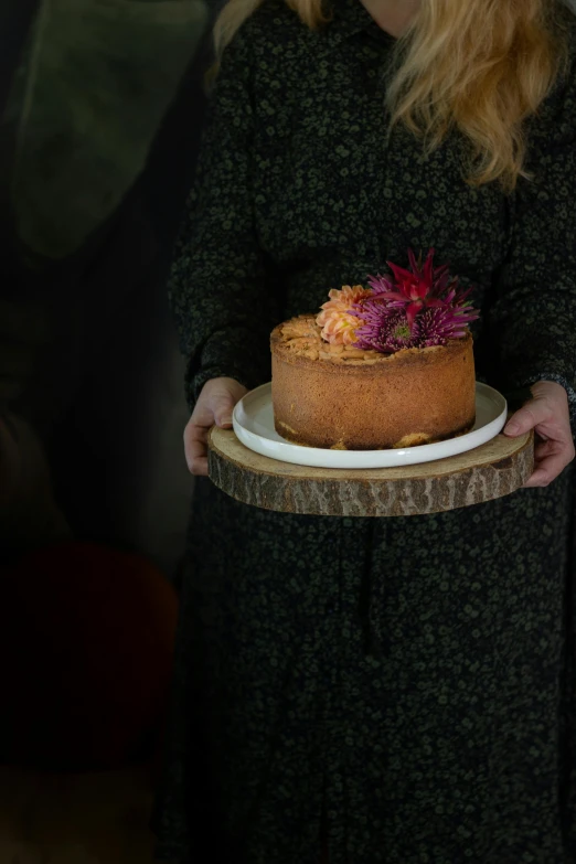 a woman holding a plate with a cake on it, a portrait, by Helen Stevenson, unsplash, made of dried flowers, standing with a black background, during autumn, large and tall