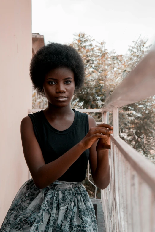 a woman standing on a balcony holding a glass of wine, by Lily Delissa Joseph, pexels contest winner, afrofuturism, black man with afro hair, concerned expression, black teenage girl, lupita nyong'o