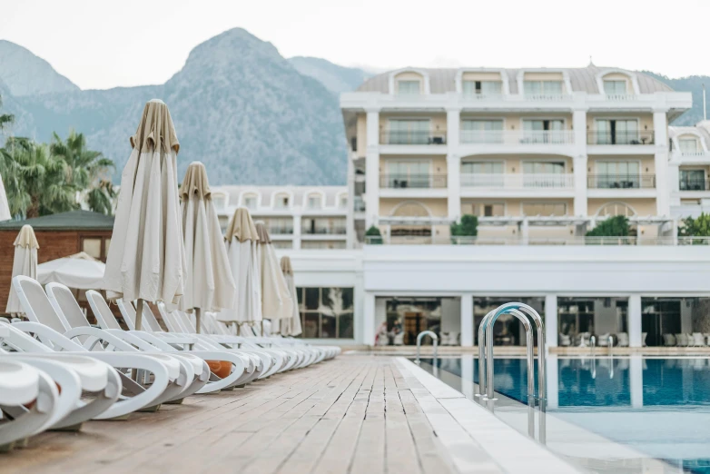 a row of lounge chairs sitting next to a swimming pool, by Carey Morris, unsplash contest winner, white marble buildings, mountains in the background, boka, hotel