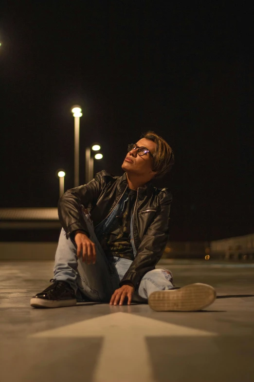 a man sitting on the ground at night, an album cover, trending on pexels, photorealism, androgynous person, wearing leather, bright sky, profile pic