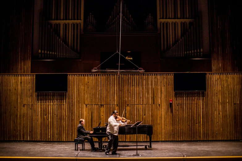 a man standing next to a piano on a stage, by James Morris, unsplash, baroque, violin, zeen chin and farel dalrymple, concert hall, a wide shot