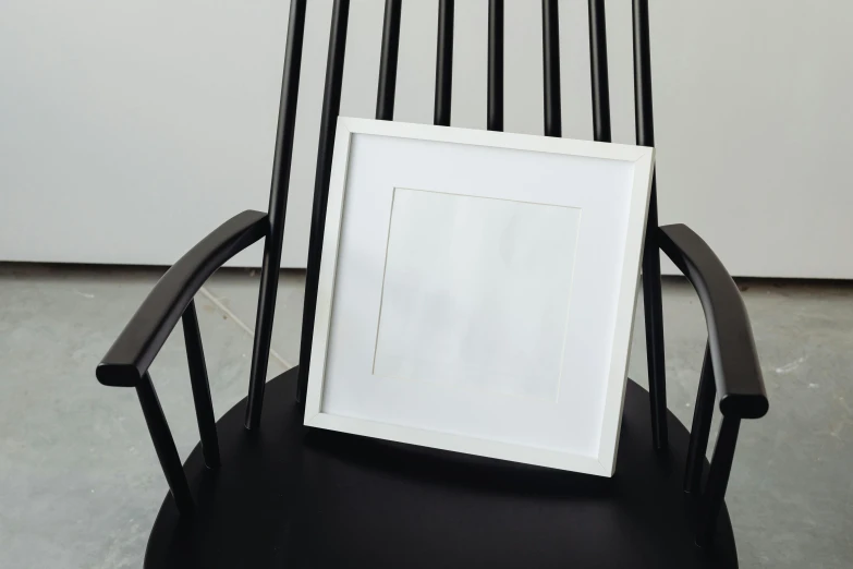 a picture frame sitting on top of a black chair, inspired by Cleve Gray, unsplash, white finish, ( ( photograph ) ), square lines, white wood