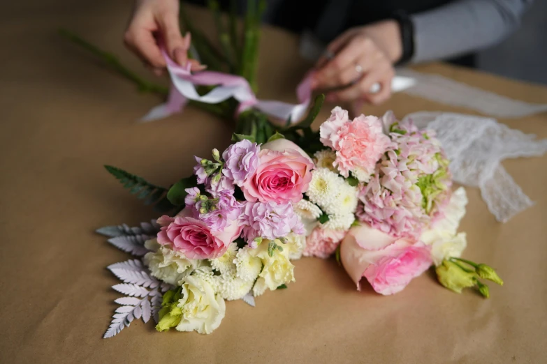 a close up of a bunch of flowers on a table, wrapped in flowers, pinks, picking up a flower, carefully crafted