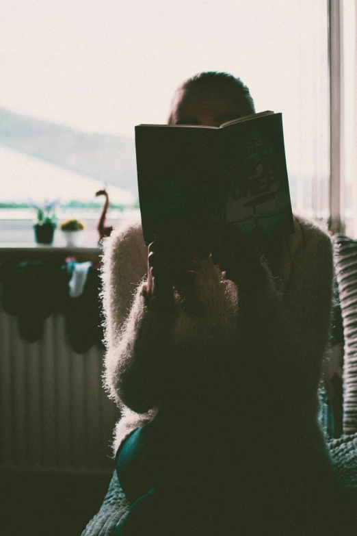 a person sitting in a chair reading a book, pexels contest winner, romanticism, snapchat photo, looking across the shoulder, hazy, holding a giant book