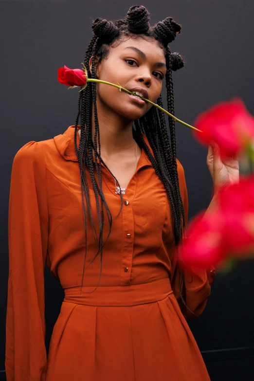 a woman holding a flower in front of her face, an album cover, inspired by Theo Constanté, trending on pexels, brown clothes, braided hair with roses, 5 0 0 px models, black and orange