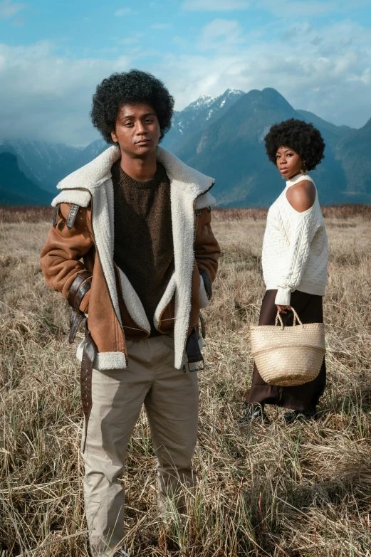 two people standing in a field with mountains in the background, inspired by Geoffrey Olsen, renaissance, wearing an aviator jacket, afro, off - white collection, brown and cream color scheme