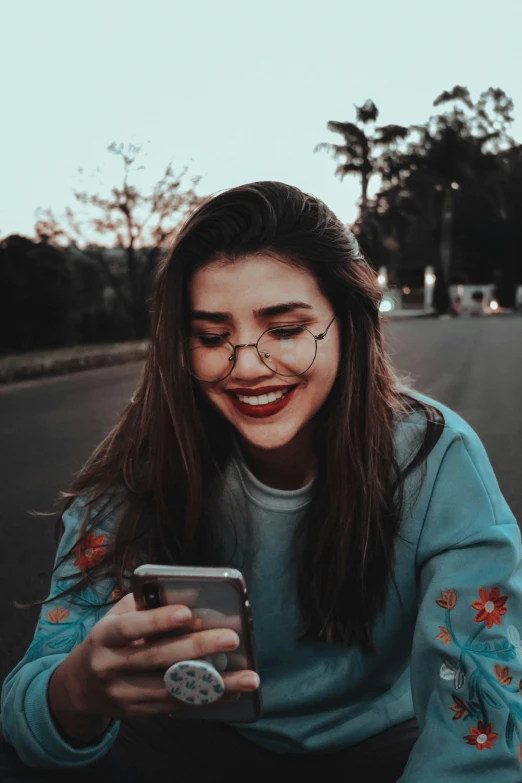 a woman sitting on the side of a road looking at her phone, trending on pexels, cheeky smile with red lips, portrait sophie mudd, dating app icon, with square glasses