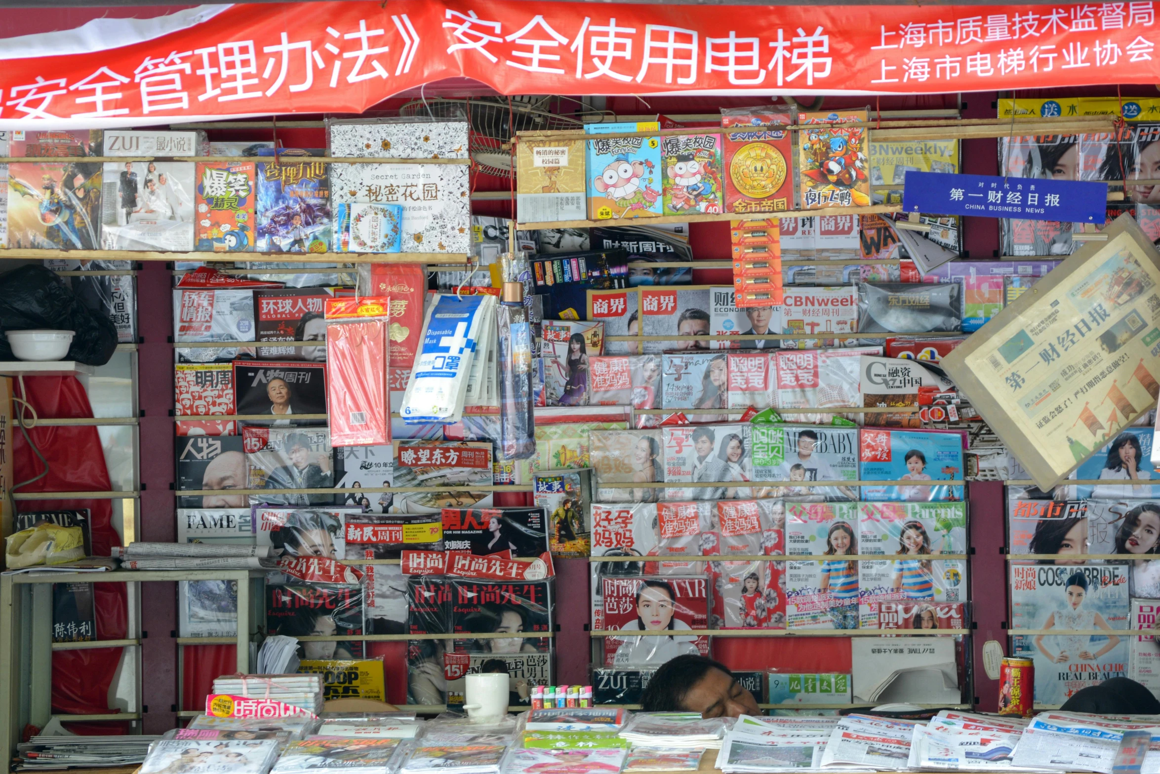 a man sitting at a table in front of a store, by Julia Pishtar, flickr, private press, overlaid with chinese adverts, textbooks and books, square, colored market stand