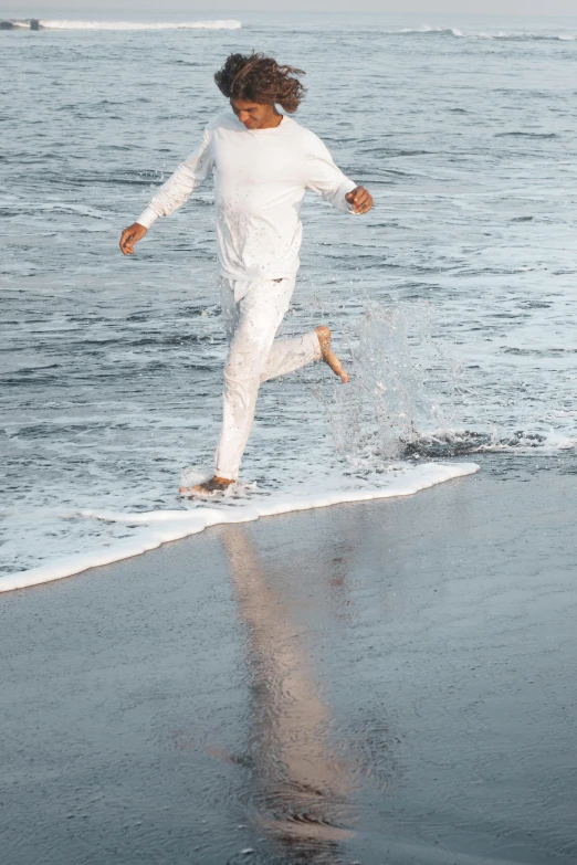 a person running on a beach near the ocean, wearing white pajamas, made purely out of water, off - white collection, oceanside