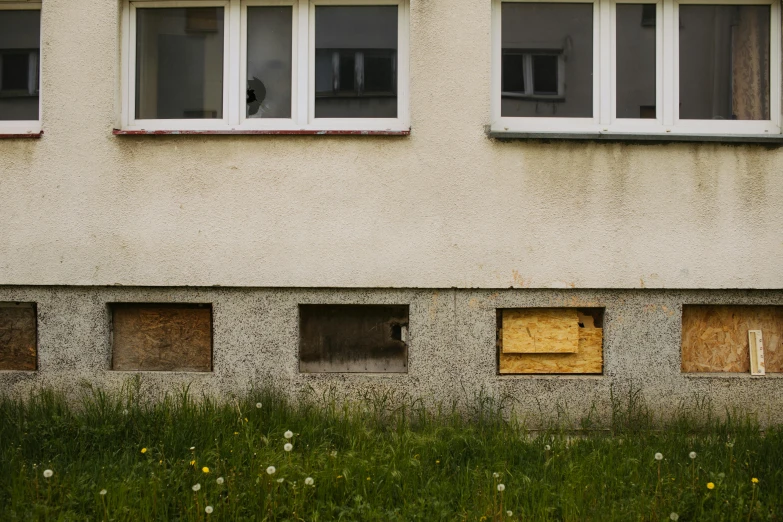 a fire hydrant in front of a building with boarded windows, by Attila Meszlenyi, postminimalism, overgrown grass, at home, brown, holes