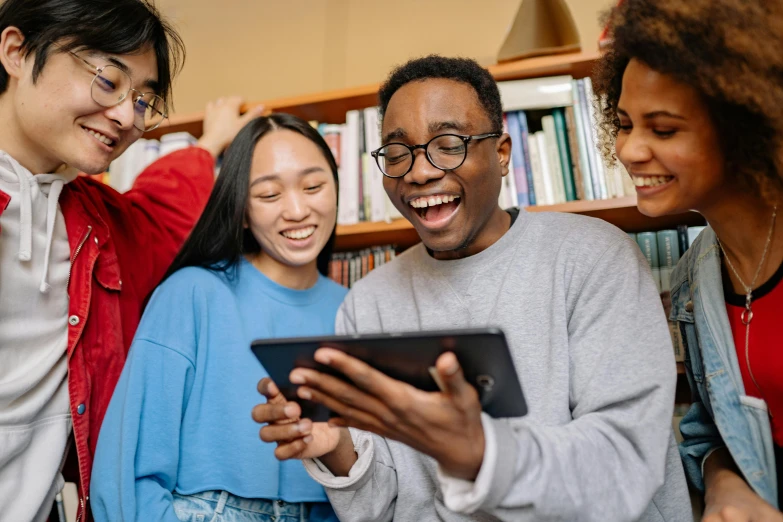 a group of people standing next to each other looking at a tablet, trending on pexels, happening, textbooks and books, very excited, pokimane, subject is smiling