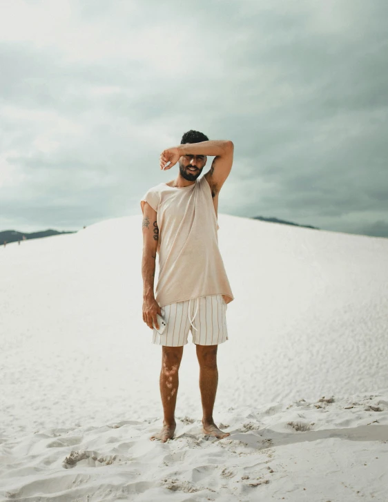 a man standing on top of a sandy beach, by Jessie Alexandra Dick, trending on unsplash, renaissance, tan skin a tee shirt and shorts, wearing toga, in front of white back drop, wearing off - white style