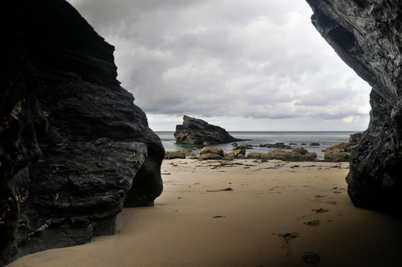a couple of large rocks sitting on top of a sandy beach, looking into a mysterious cave, cornwall, slight overcast, today\'s featured photograph 4k
