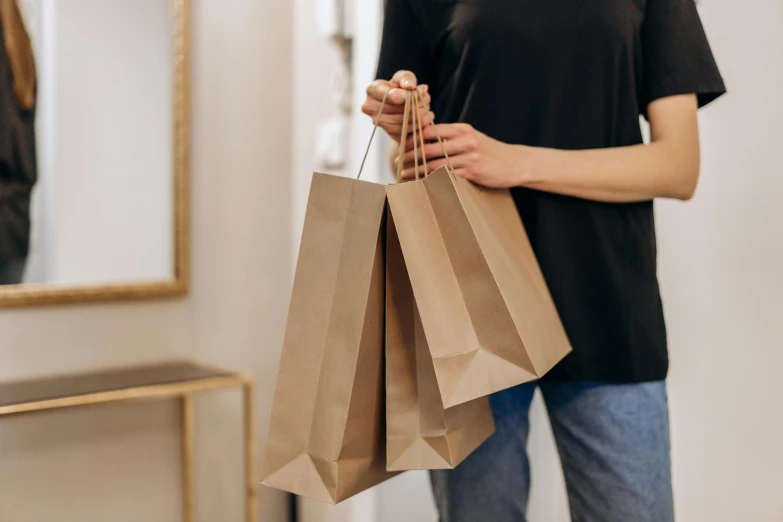 a woman holding shopping bags in front of a mirror, pexels contest winner, brown paper, 🦩🪐🐞👩🏻🦳, wearing pants and a t-shirt, rituals