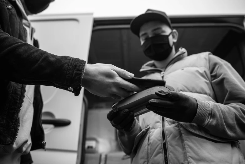 a couple of men standing next to each other, a black and white photo, by Adam Marczyński, pexels, graffiti, delivering parsel box, wearing facemask, scanning items with smartphone, truck