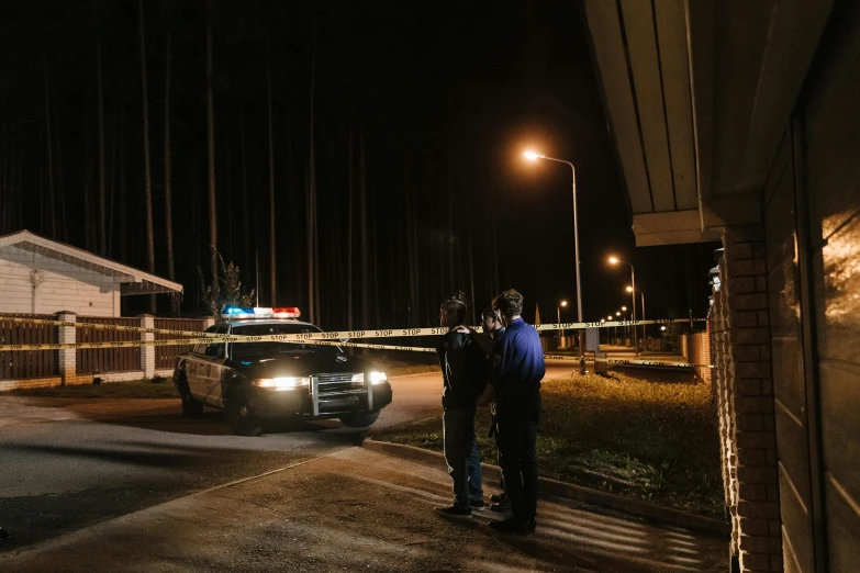 a couple of men standing next to a police car, by Everett Warner, pexels contest winner, hurufiyya, large windows to forest at night, police tape, in front of a garage, espoo