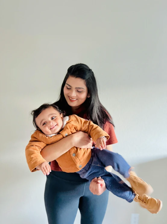 a woman holding a child in her arms, by Olivia Peguero, pexels contest winner, happy wise. he has bouncy belly, a portrait of rahul kohli, plain background, indoor picture