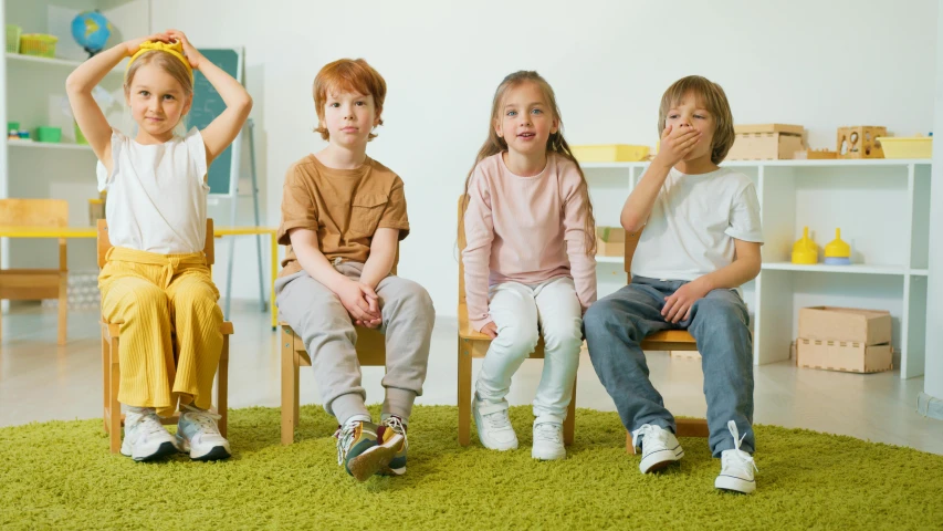 a group of children sitting on top of a green rug, sitting on a chair