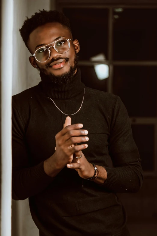 a man with glasses standing next to a wall, an album cover, inspired by David Bailly, trending on pexels, black main color, cute young man, elegantly dressed, christian