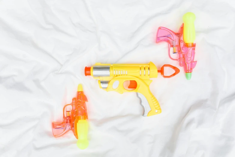 a couple of water guns laying on top of a bed, yellow, multi - coloured