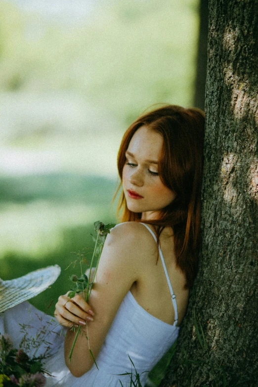a woman in a white dress sitting under a tree, an album cover, inspired by Konstantin Somov, pexels contest winner, ( redhead, sleepy feeling, ellie bamber fairy, candid portrait photo