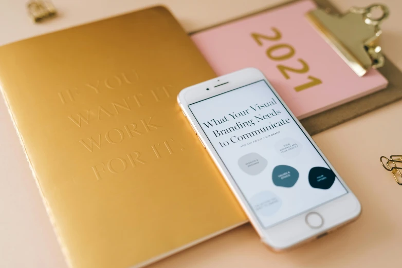 a cell phone sitting on top of a desk next to a notebook, by Julia Pishtar, trending on pexels, white and gold color palette, graphic design contest winner, 2 0 2 2 photo, magazine design