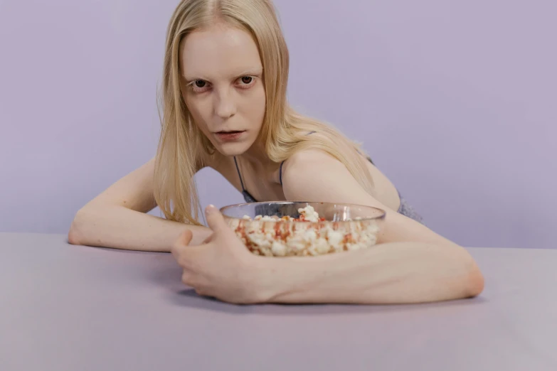a woman sitting at a table with a bowl of food, an album cover, inspired by Vanessa Beecroft, trending on pexels, magic realism, looks a blend of grimes, crystal castles, still from a movie, showstudio