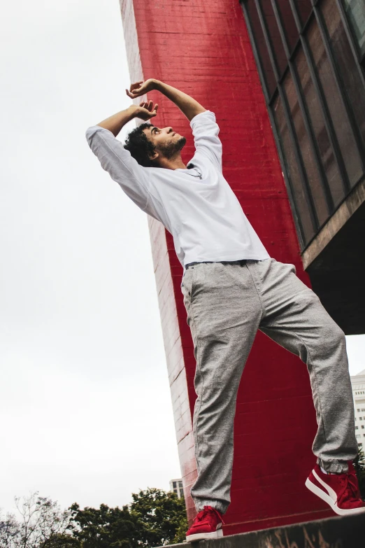 a man standing on a skateboard in front of a building, inspired by Camilo Egas, arabesque, wearing a linen shirt, men look up at the sky, red and grey only, baggy pants