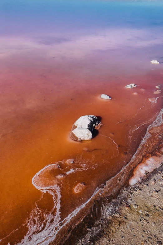 a body of water that has some rocks in it, pink and orange, red dust, aerial, manuka