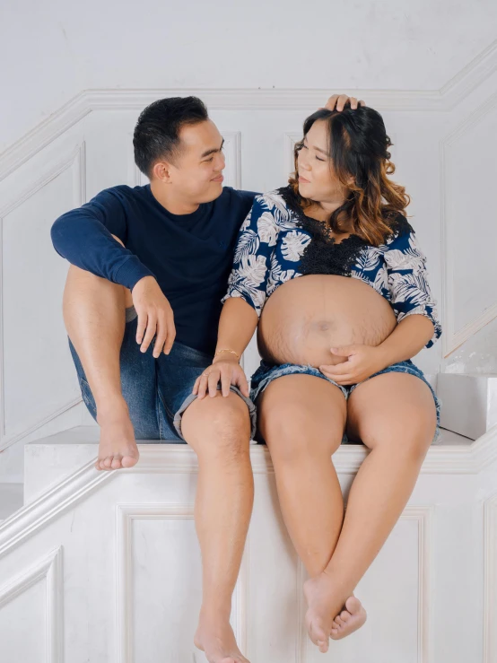 a man and a woman sitting next to each other, a colorized photo, by Basuki Abdullah, pexels contest winner, hyperrealism, pregnant belly, in front of white back drop, gif, balcony