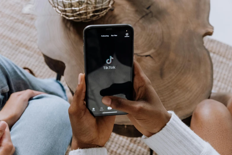 a person sitting on a couch holding a cell phone, trending on pexels, tachisme, black and teal paper, trending on tiktok, corporate phone app icon, charcoal color skin