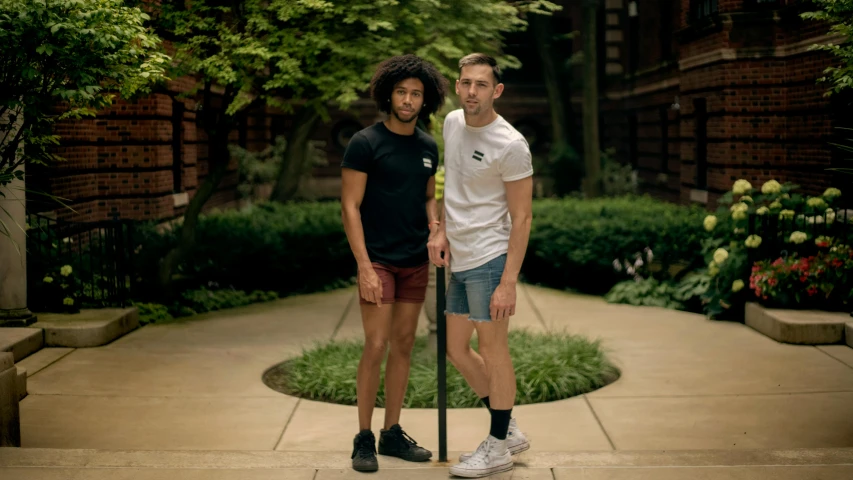 a couple of men standing next to each other on a sidewalk, by Andrew Stevovich, tan skin a tee shirt and shorts, pride month, neo rauch and nadav kander, shows a leg