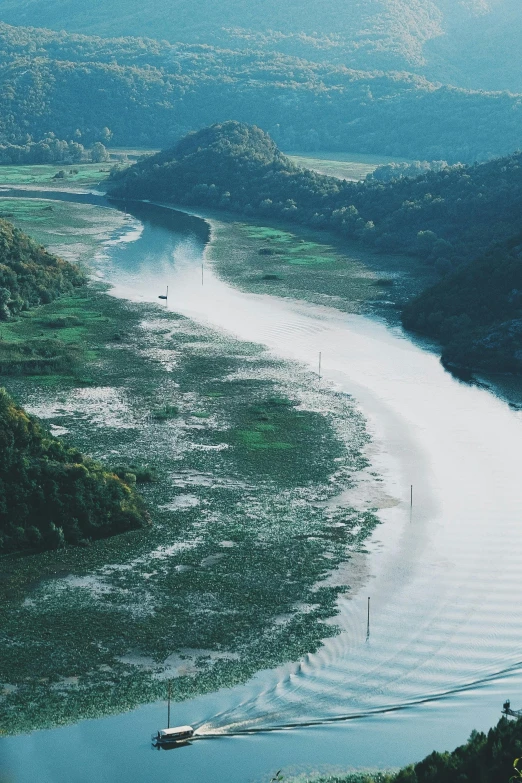 a boat traveling down a river next to a lush green hillside, an album cover, unsplash contest winner, hurufiyya, turkey, river delta, new zeeland, wide high angle view