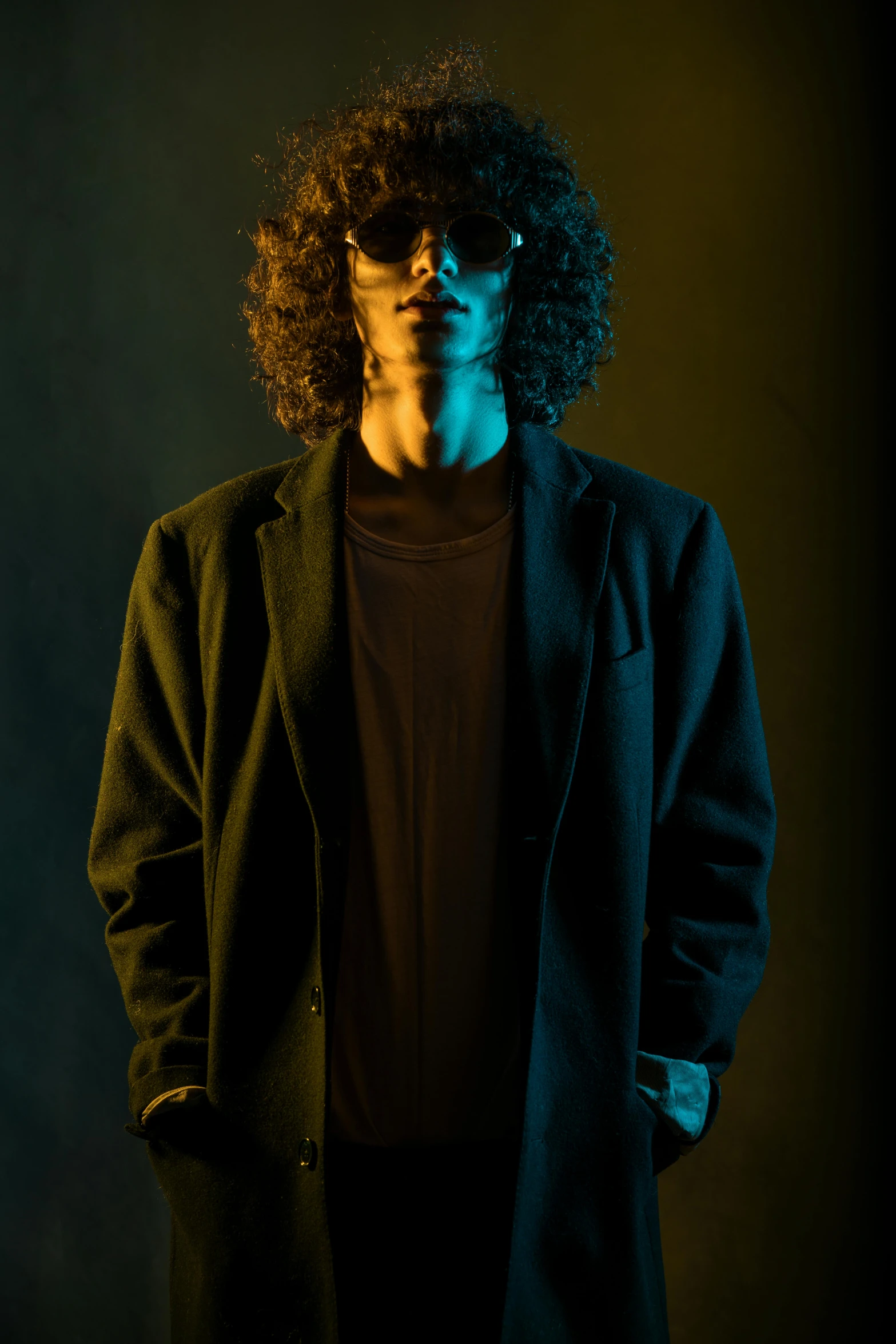 a man standing in front of a black background, an album cover, trending on pexels, fashion model in sunglasses, curly haired, dramatic lighting; 4k 8k, an edgy teen assassin