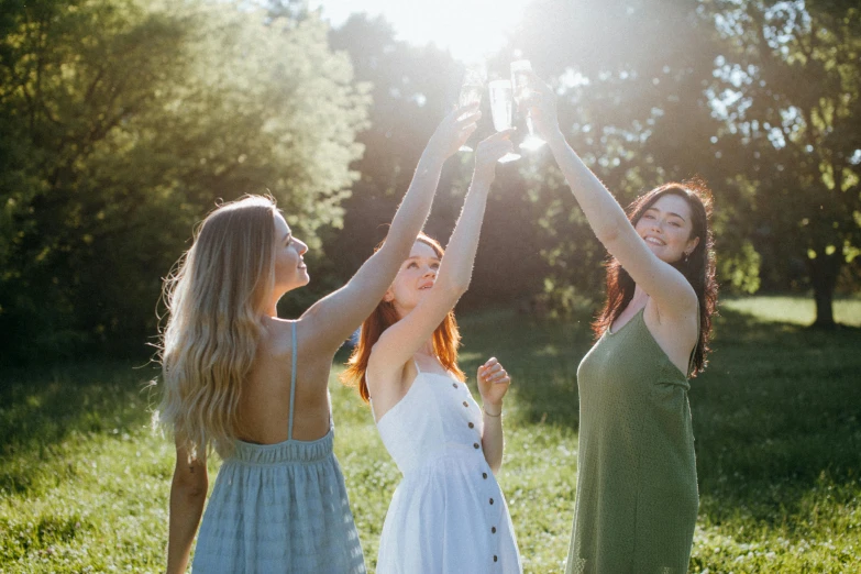 a group of women standing on top of a lush green field, by Emma Andijewska, pexels contest winner, renaissance, holding glass of wine, sun flare, rituals, three women