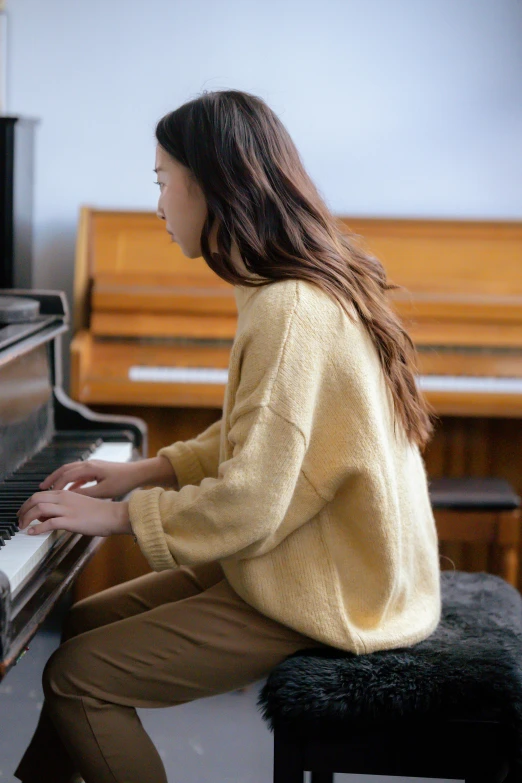 a woman sitting on a stool playing a piano, trending on pexels, wearing casual sweater, wearing wheat yellow gauze, aoi ogata, beige