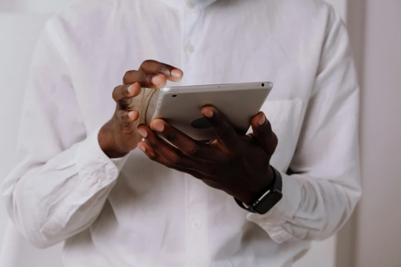 a close up of a person holding a tablet, by Carey Morris, trending on pexels, black man, wearing a white blouse, holding a very advance phone, grayish