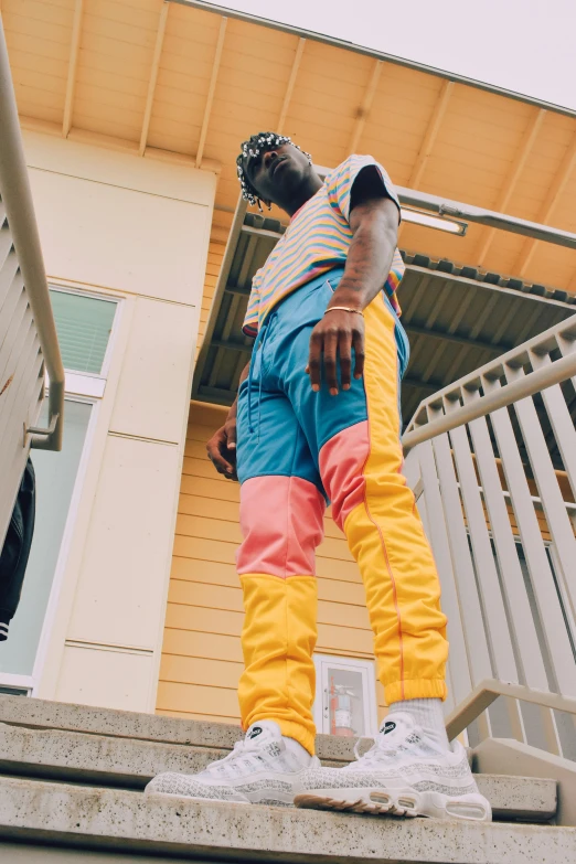 a man standing on the steps of a building, an album cover, trending on pexels, happening, in blue and yellow clothes, baggy pants, cool offset colors, looking off into the sunset