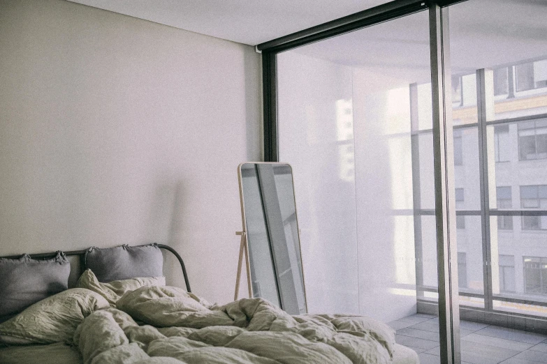 a bed sitting in a bedroom next to a window, unsplash, postminimalism, standing in front of a mirror, low quality photo, nesting glass doors, dull colours