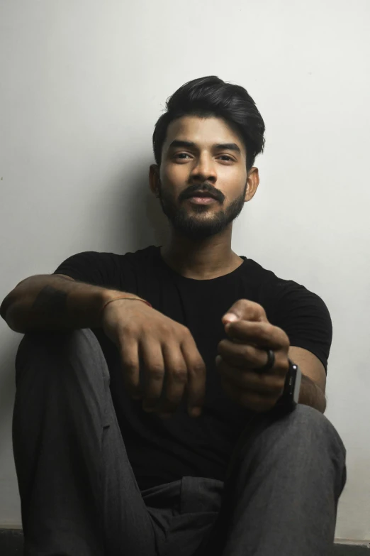 a man sitting on the ground holding a cell phone, an album cover, pexels contest winner, hurufiyya, a portrait of rahul kohli, non binary model, headshot profile picture, he is wearing a black t-shirt