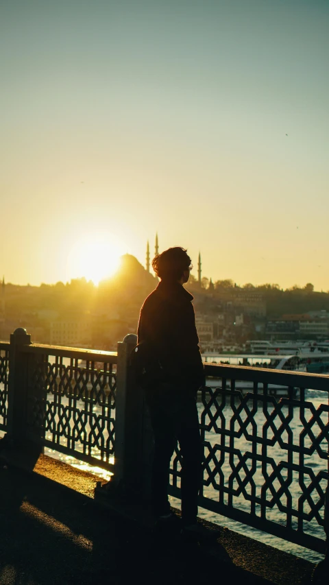 a man standing on top of a bridge next to a body of water, istanbul, golden hour 8k, low quality photo