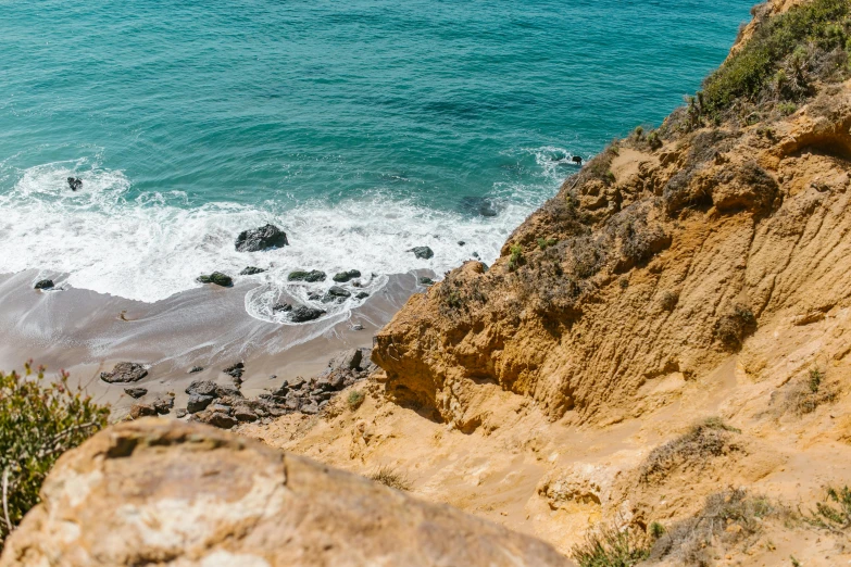 a man standing on top of a cliff next to the ocean, by Kristin Nelson, unsplash, hollister ranch, ocher and turquoise colors, half submerged in heavy sand, climbing up a cliffside