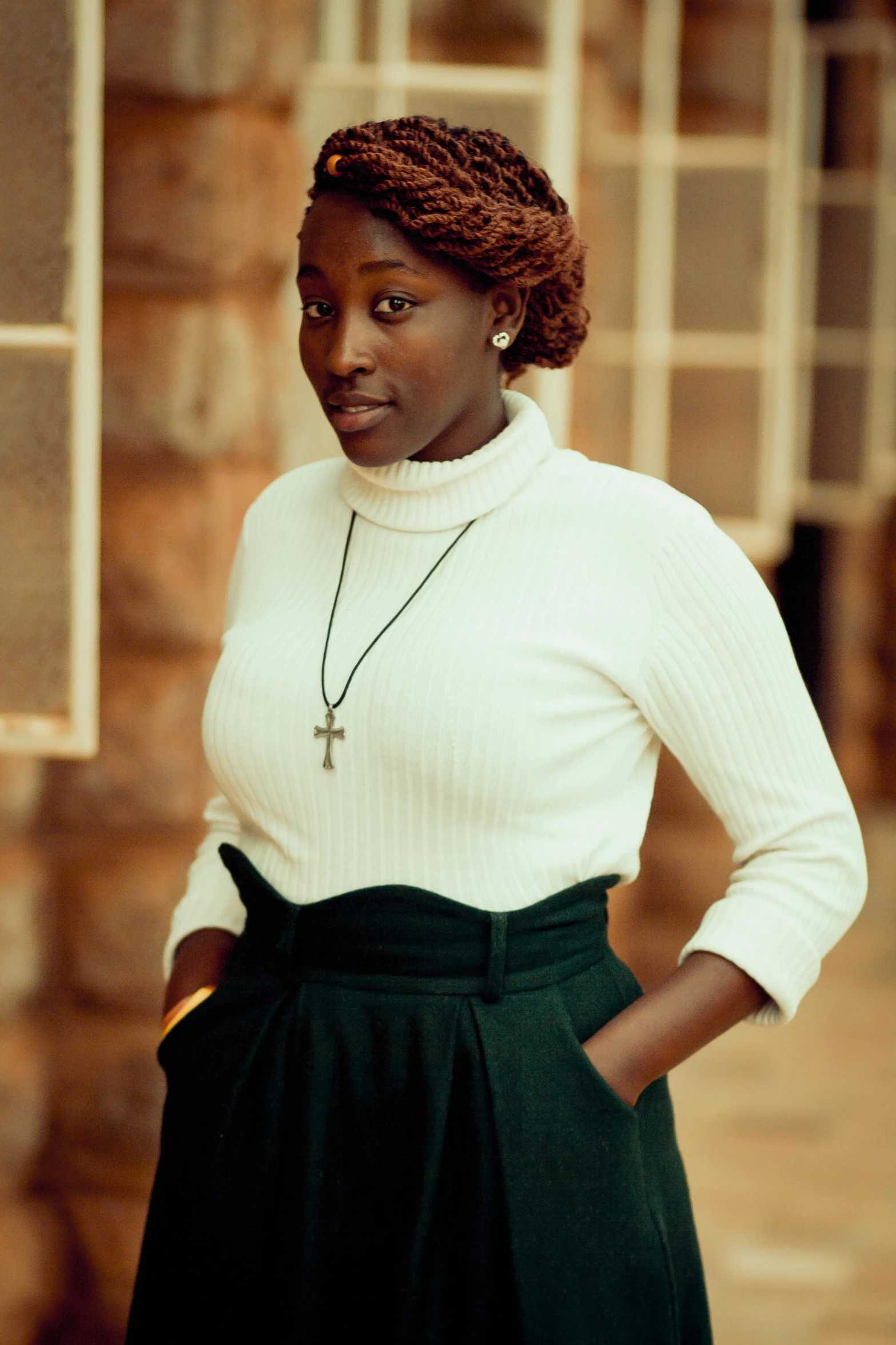 a woman standing in front of a brick building, by Chinwe Chukwuogo-Roy, trending on pexels, renaissance, in white turtleneck shirt, white shirt and green skirt, wears a egyptian ankh necklace, studio photo