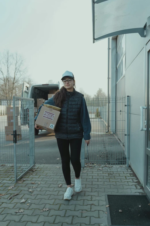 a woman walking down a sidewalk carrying a box, by Andries Stock, pexels contest winner, arbeitsrat für kunst, low quality video, in front of a garage, full body cute young lady, van