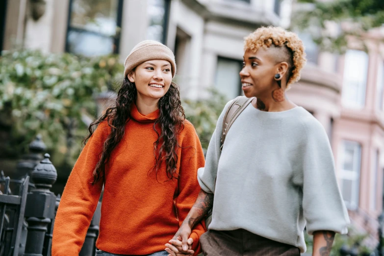 two women walking down a city street holding hands, trending on pexels, long orange sweatshirt, diverse ages, lesbian embrace, background image